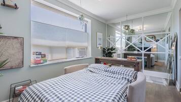 A bedroom with a bed, a window with blinds, a bedside table, and a mirror.