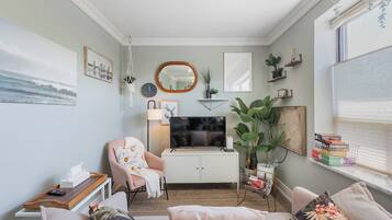A cozy living room with a sofa, armchair, and a television on a cabinet.