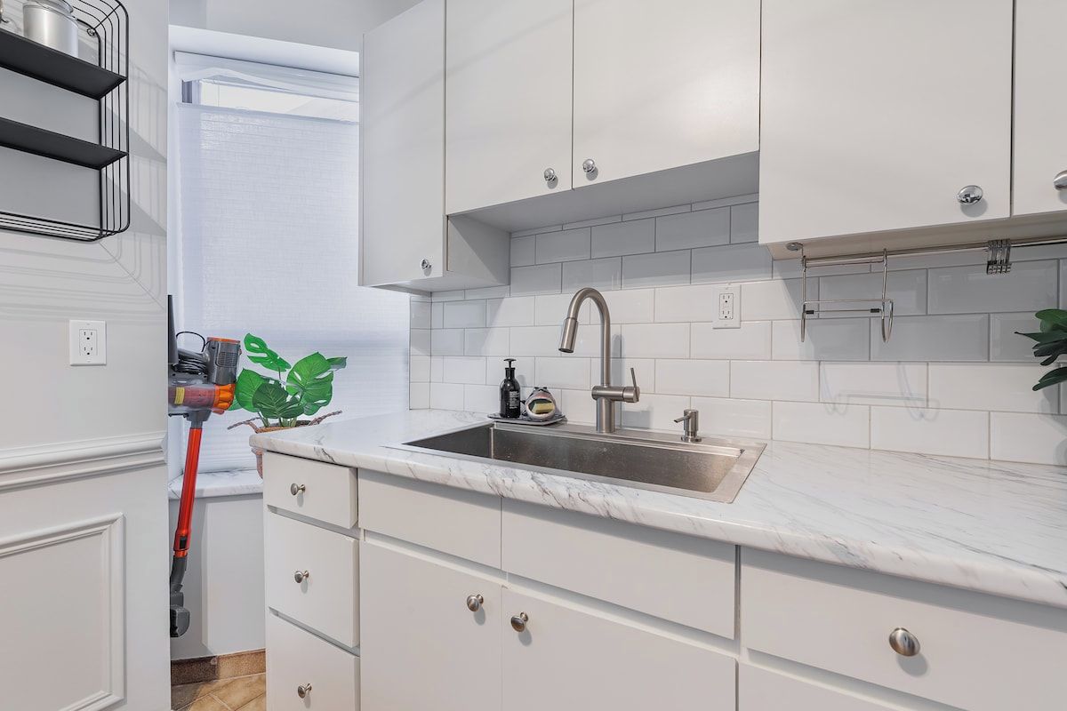 A modern kitchen with white cabinetry, a marble countertop, and a stainless steel sink.