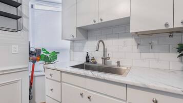 A modern kitchen with white cabinetry, a marble countertop, and a stainless steel sink.