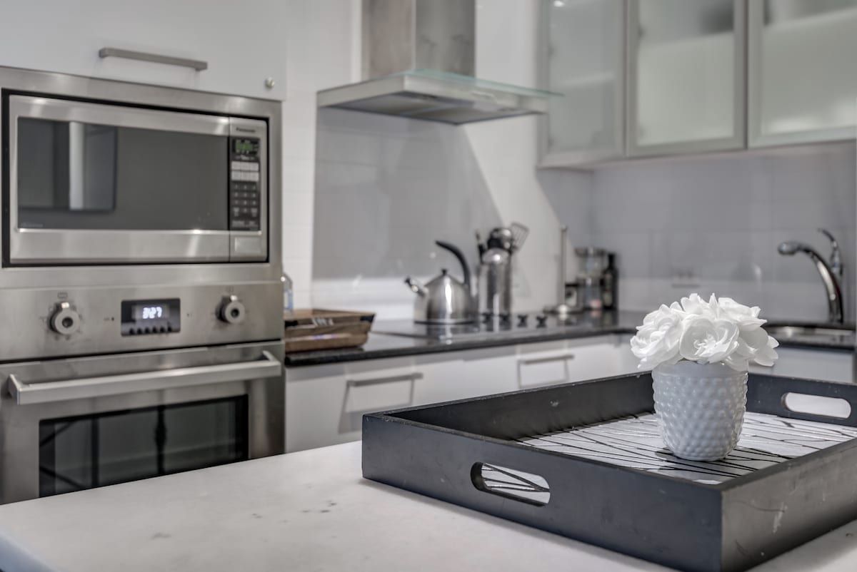 Een moderne keuken met roestvrijstalen apparatuur, een glazen spatwand en een schaal met een witte keramieken pot op het aanrecht.