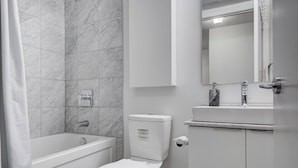 A bathroom with a bathtub, toilet, and a vanity with a mirror. - Stylish 1Bed Den Unit in the heart of Dt (Toronto)