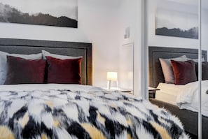 Une chambre d’hôtel avec un grand lit, deux tables de chevet, une petite table, une lampe et un miroir.