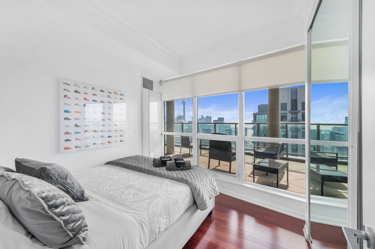 A modern bedroom with a large window, a bed with grey bedding, and a city view.
