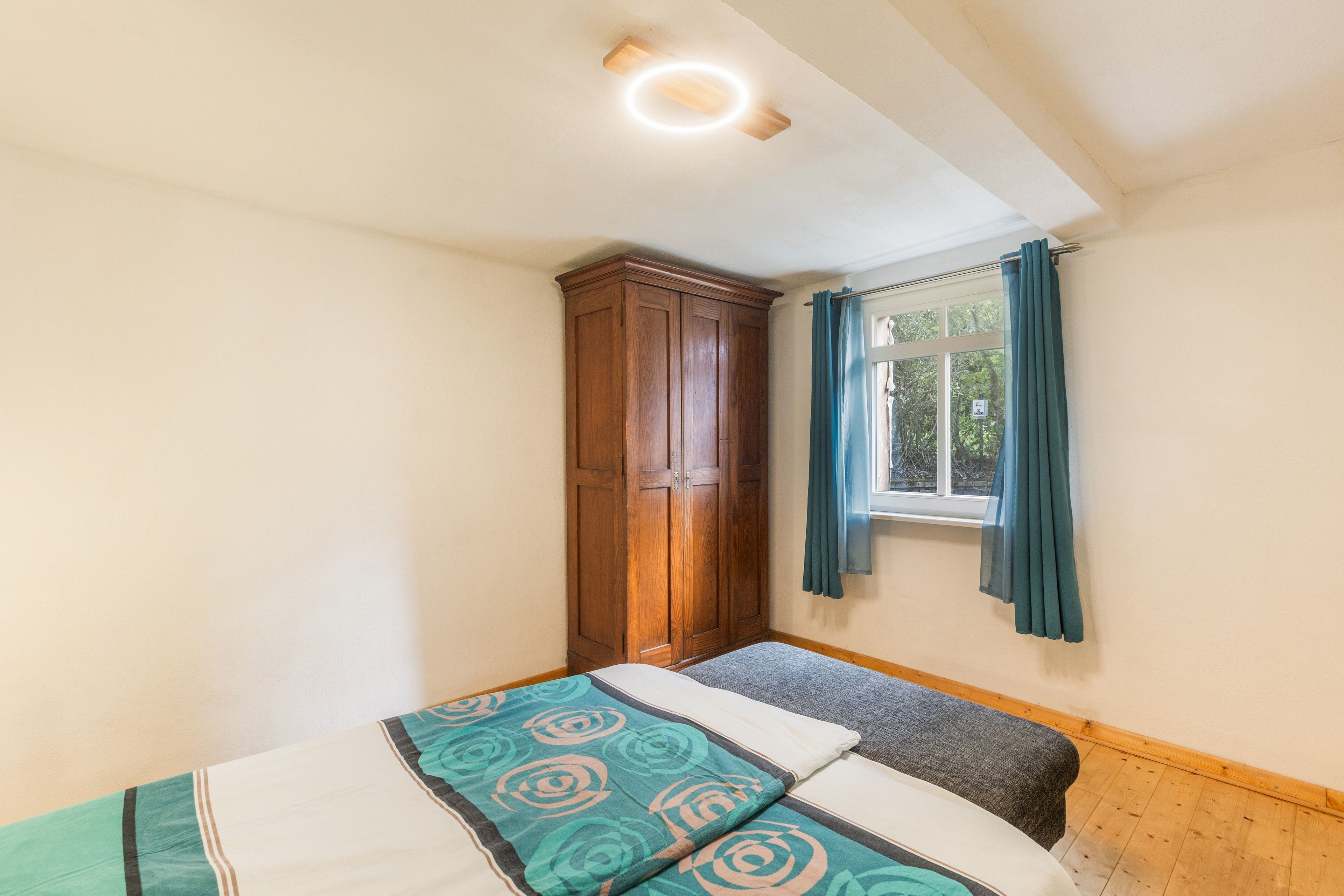 A bedroom with a bed, a wardrobe, a window with curtains, and a ceiling light.