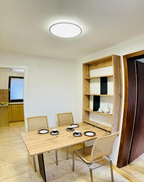 Un coin repas avec une table et des chaises en bois, un luminaire au plafond et une bibliothèque avec des étagères.