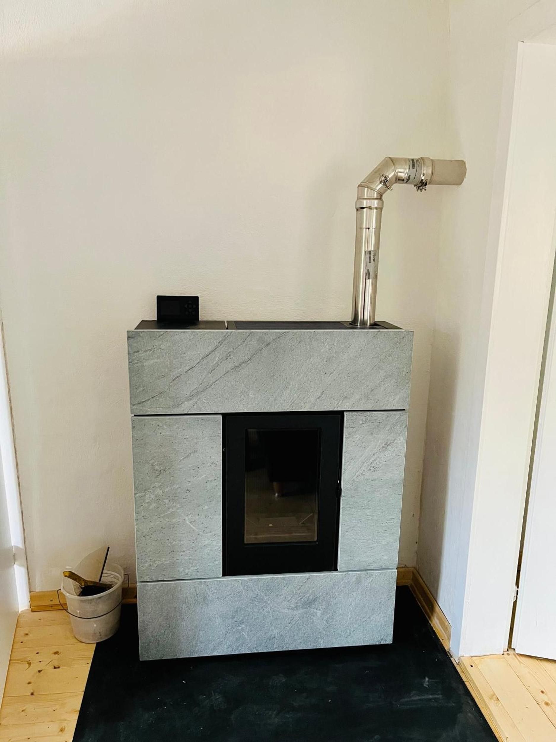 Ein moderner Kamin mit Steinverkleidung und einer Tür aus schwarzem Glas, vor einer schlichten Wand.