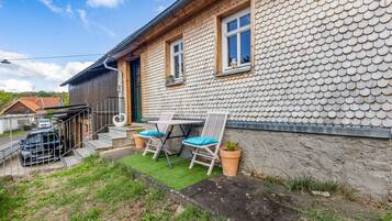 A house with a unique tiled exterior, a small patio with two chairs and a table, and a car parked outside.