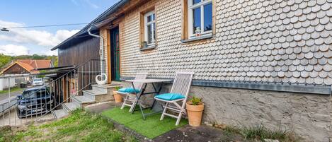 A house with a unique tiled exterior, a small patio with two chairs and a table, and a car parked outside.