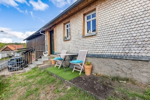 A house with a unique tiled exterior, a small patio with two chairs and a table, and a car parked outside.