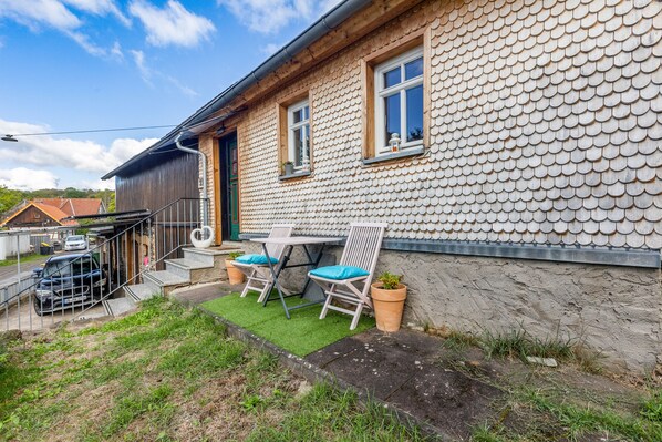 A house with a unique tiled exterior, a small patio with two chairs and a table, and a car parked outside.