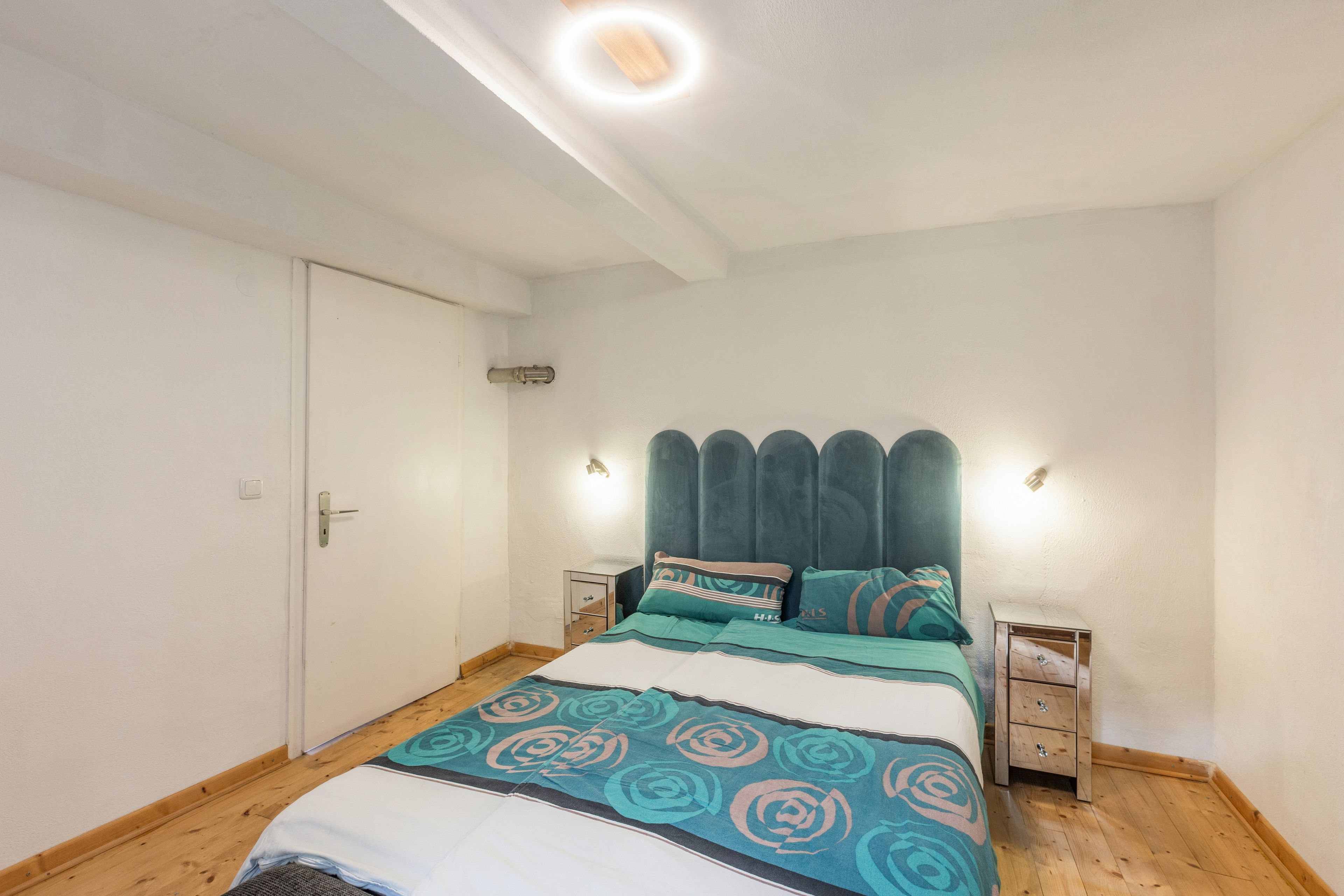 Ein Schlafzimmer mit einem Bett, Nachttischen, einer Tür und einer Lampenleuchte.