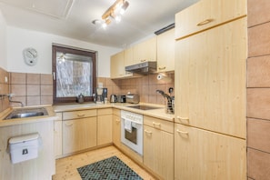 A compact kitchen with wooden cabinets, a built-in oven, a coffee maker, and a window with blinds.