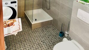 A compact bathroom with a shower, toilet, and washing machine. - Holiday Home 'Ferienhaus Im Grünen Mit Garten' with Private Garden and Wi-Fi (Schotten)