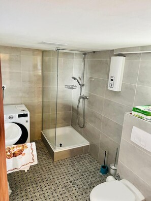 Et lille badeværelse med bruser, toilet og vaskemaskine.