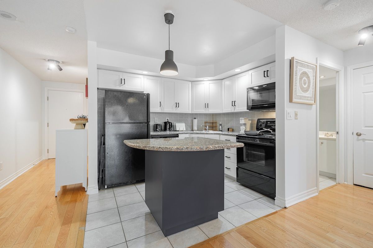 A modern kitchen with white cabinets, a granite countertop island, and stainless steel appliances.