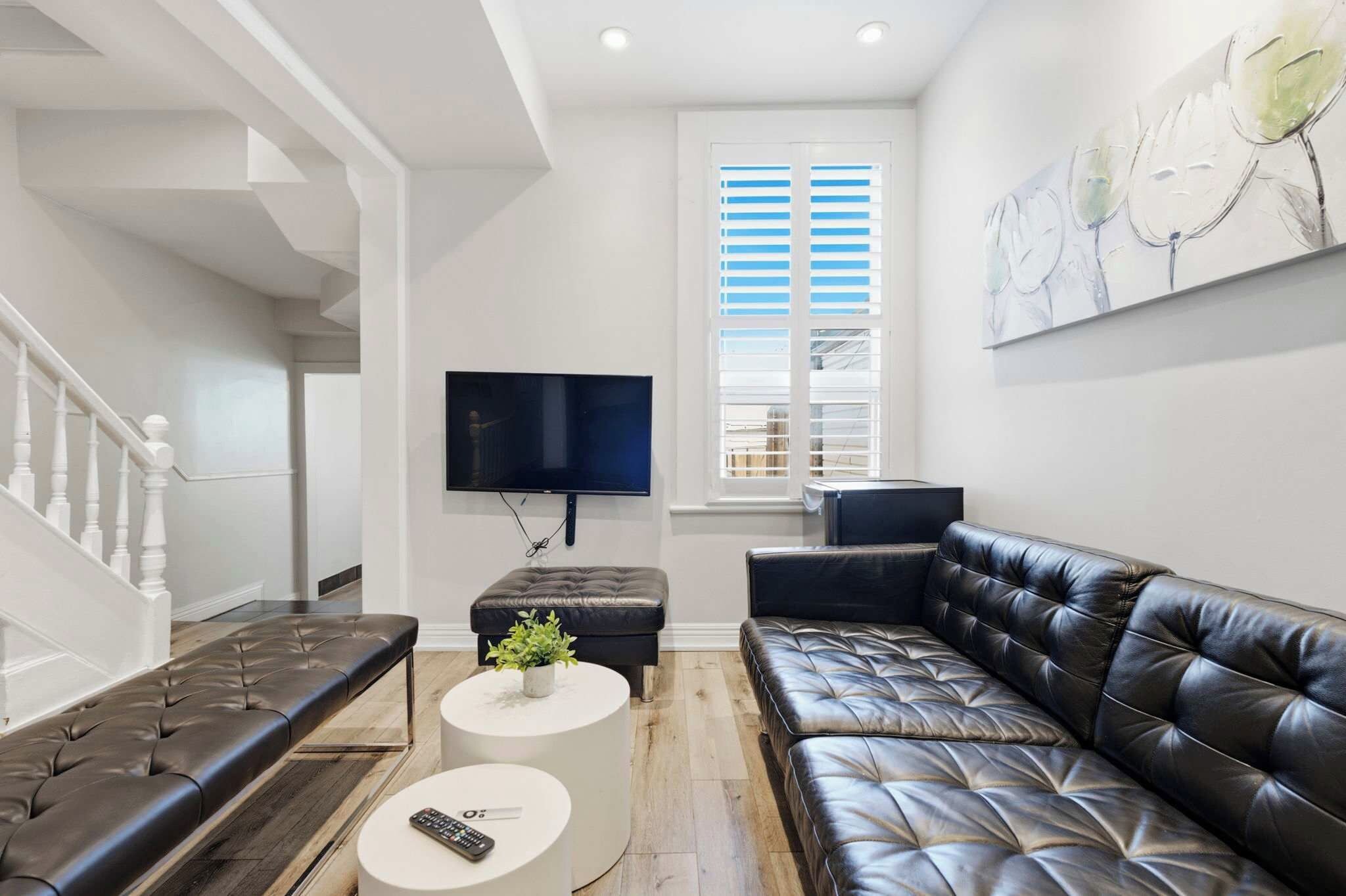 A modern living room with a black leather sofa, a white coffee table, and a flat-screen TV mounted on the wall.