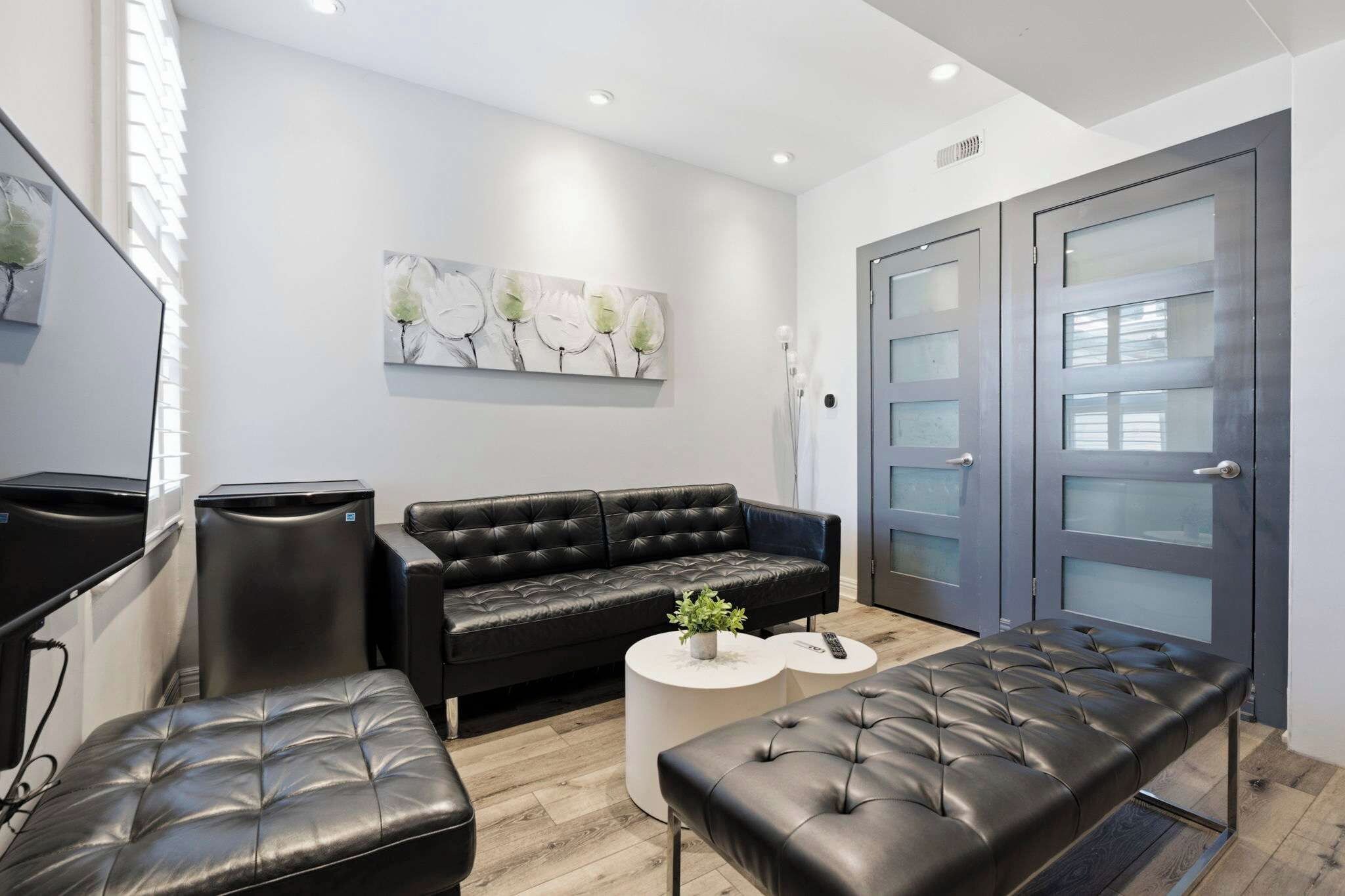 A modern room with a black leather sofa, a matching ottoman, a small white side table, and a grey door with glass panels.