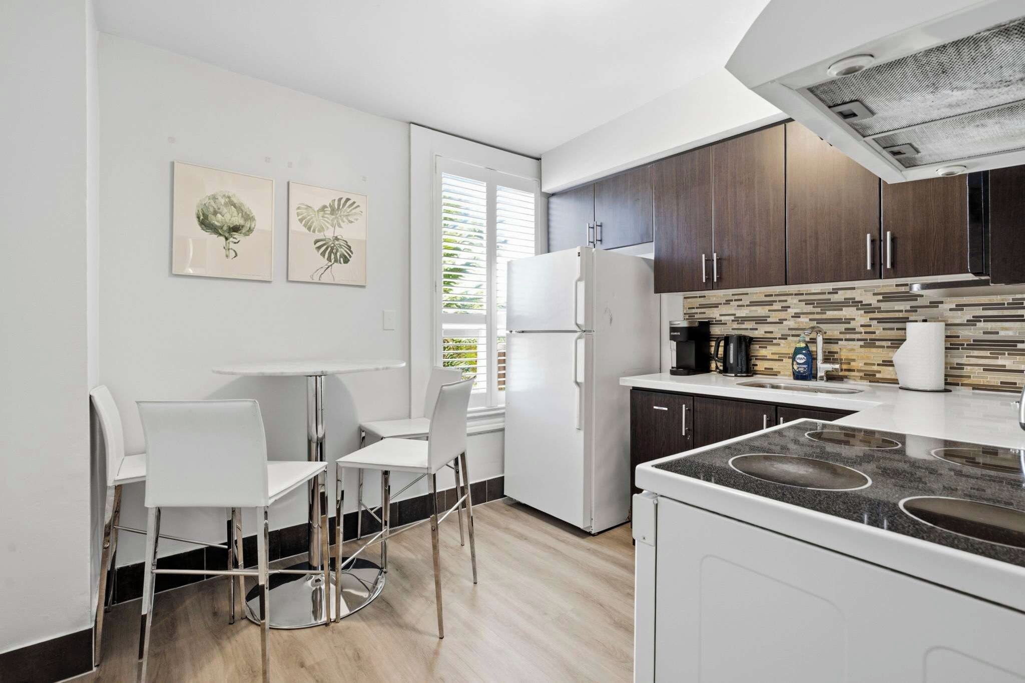 A modern kitchen with a built-in stove, white cabinetry, and a dining area with white chairs.