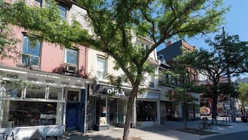 A street lined with multi-story buildings, storefronts, and a tree providing shade.