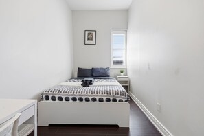A narrow room with a bed, a small bedside table, a window with blinds, and a wall-mounted picture. - Spacious 4BR Toronto Stay Near U of T & Downtown (Toronto)