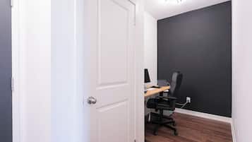 Una habitación con una puerta blanca, un escritorio con una computadora y una silla, y una pared oscura.