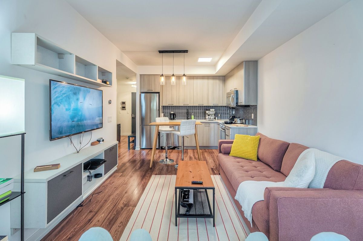 Una sala moderna con un televisor de pantalla plana, una mesa de centro de madera y un sofá con un cojín amarillo.