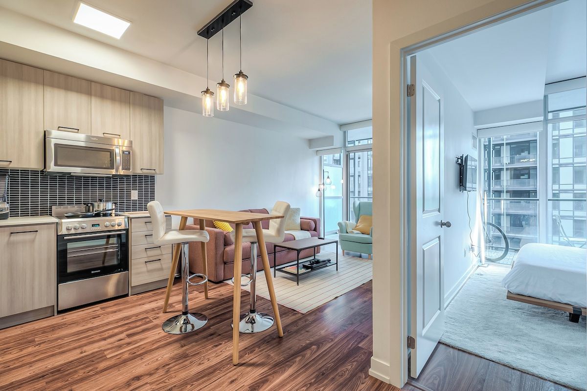 Una cocina moderna con electrodomésticos de acero inoxidable, un comedor con mesa y sillas de madera, y un amplio ventanal que proporciona luz natural.