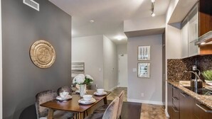 Una cucina moderna con mobili scuri, un piano di lavoro in granito e una zona pranzo con tavolo e sedie in legno.