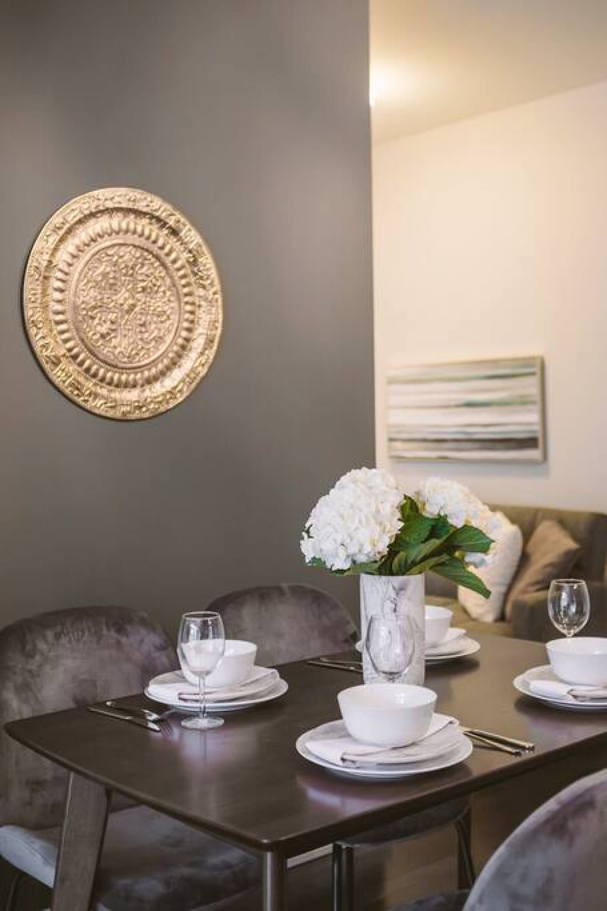 Ein Essbereich mit einem Tisch für vier Personen, einer Vase mit weißen Blumen und einem dekorativen Teller an der Wand.