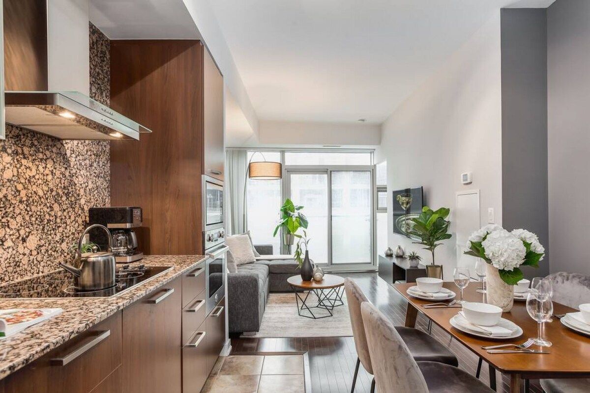 Una cocina moderna con encimeras de granito, estufa integrada y comedor con una mesa lista para dos comensales.
