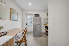 A compact kitchen with a refrigerator, microwave, and a dining area with a wooden table and chairs. - Cozy Studio w/ Fast WiFi, Parking & Workspace (Toronto)
