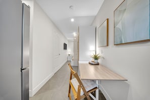 A modern kitchen with a refrigerator, a wooden dining table, and a chair. - Cozy Studio w/ Fast WiFi, Parking & Workspace (Toronto)