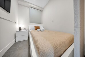 A small, modern bedroom with a bed, bedside table, and a window with blinds. - Cozy Studio w/ Fast WiFi, Parking & Workspace (Toronto)