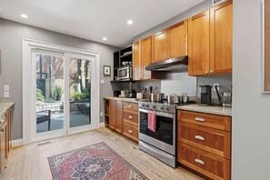 A kitchen with wooden cabinets, a built-in microwave, a stove, and a large sliding glass door leading to an outdoor area. - Remodeled 2BR Victorian Gem Near Queen West (Toronto)