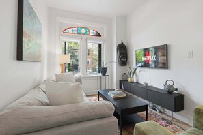 A living room with a sofa, coffee table, TV, and a bookshelf. - Remodeled 2BR Victorian Gem Near Queen West (Toronto)