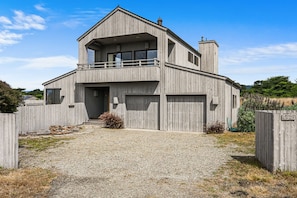 A two-story house with a balcony, a garage, and a gravel driveway. - Ocean Song Main | Peak Ocean View, Bluff Trail (Sea Ranch)