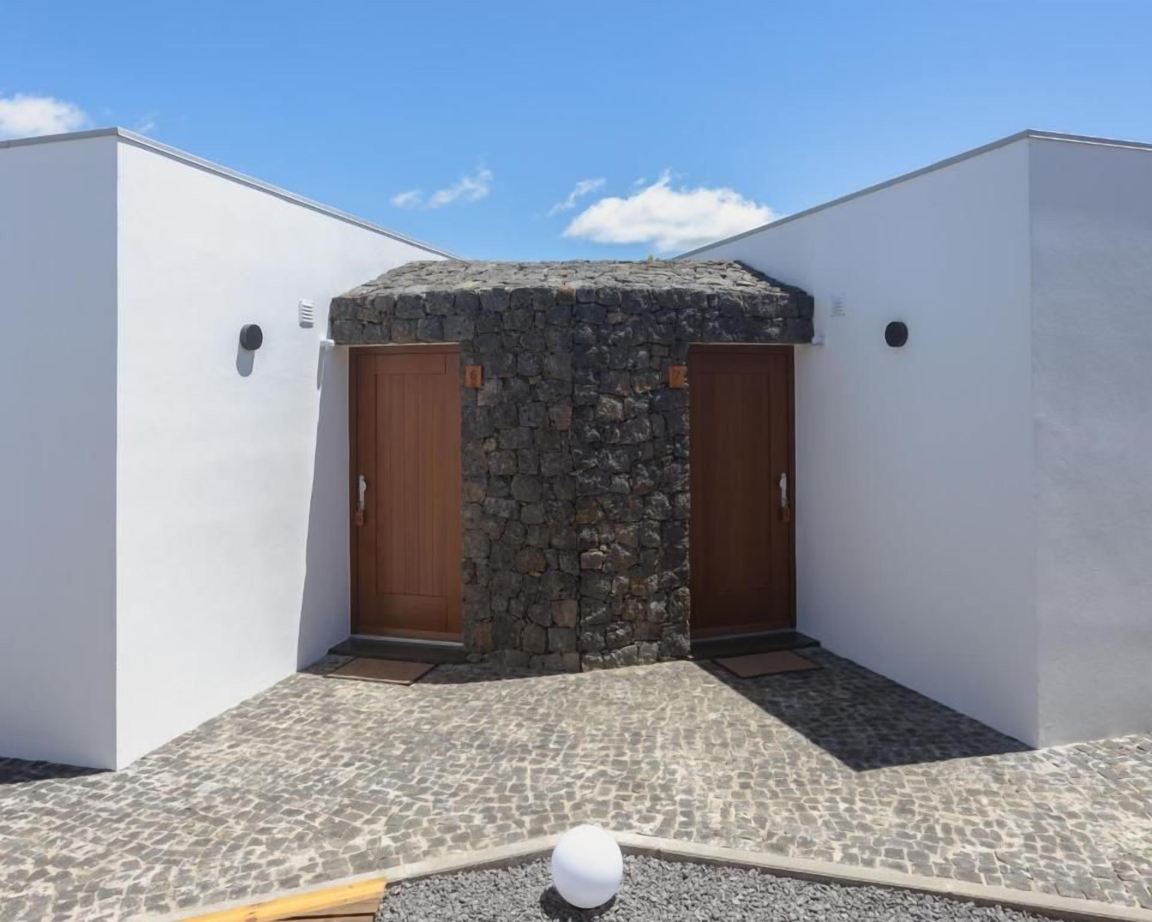 A building with two wooden doors, a stone wall, and a tiled ground.