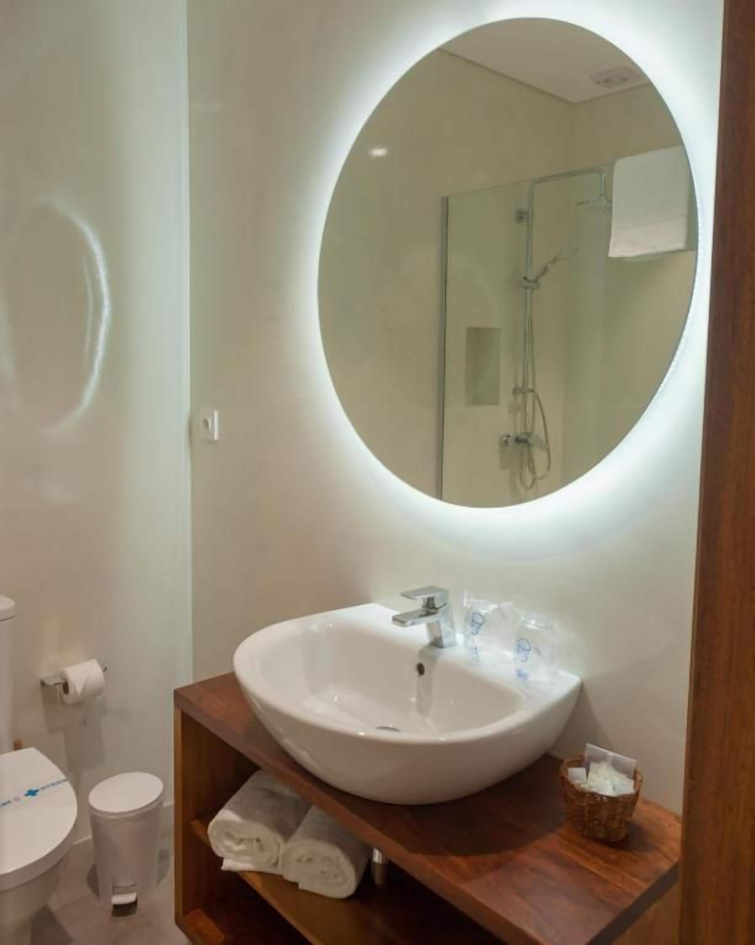 Un baño con un espejo redondo, un lavabo blanco y un mueble de tocador de madera.