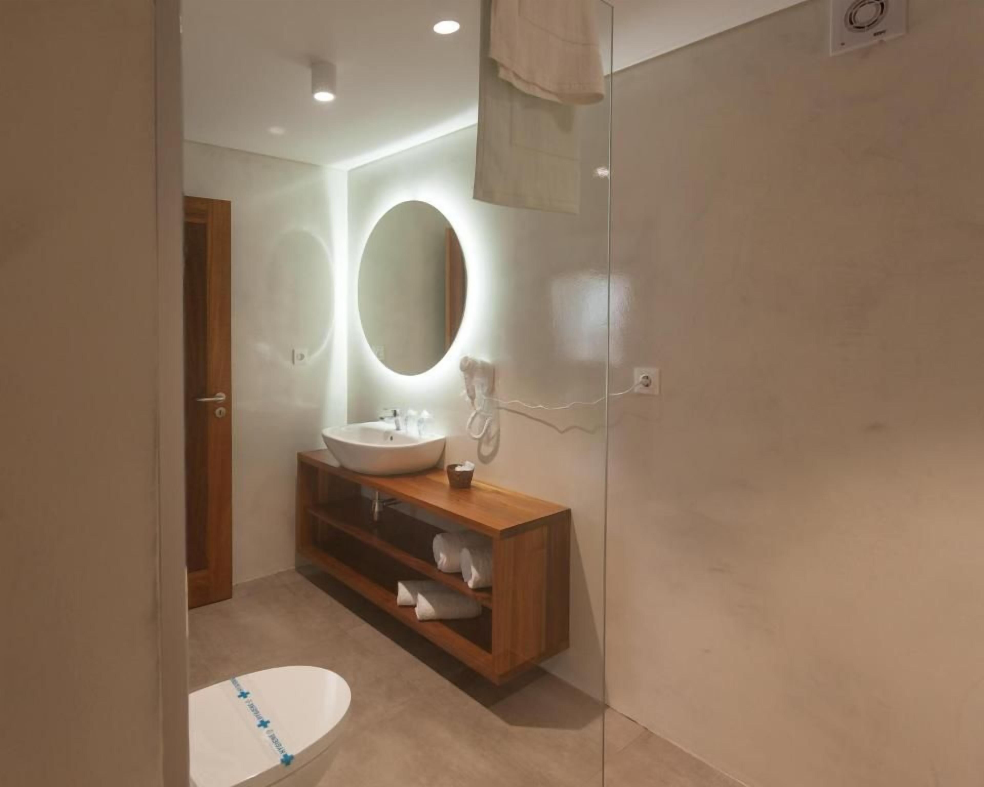 Ein modernes Badezimmer mit einem Holzkosmetikschrank, einem runden Spiegel und einem weißen Waschbecken.