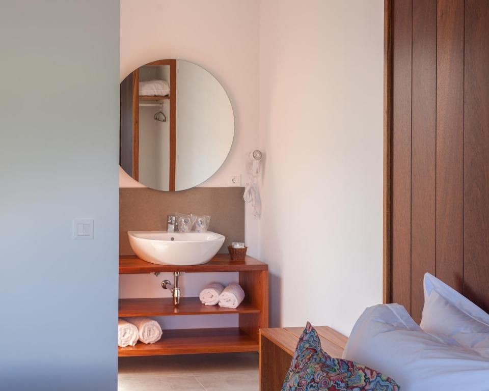 Een slaapkamer met een bed, een houten nachtkastje, een witte wastafel, een spiegel en een plank met handdoeken.