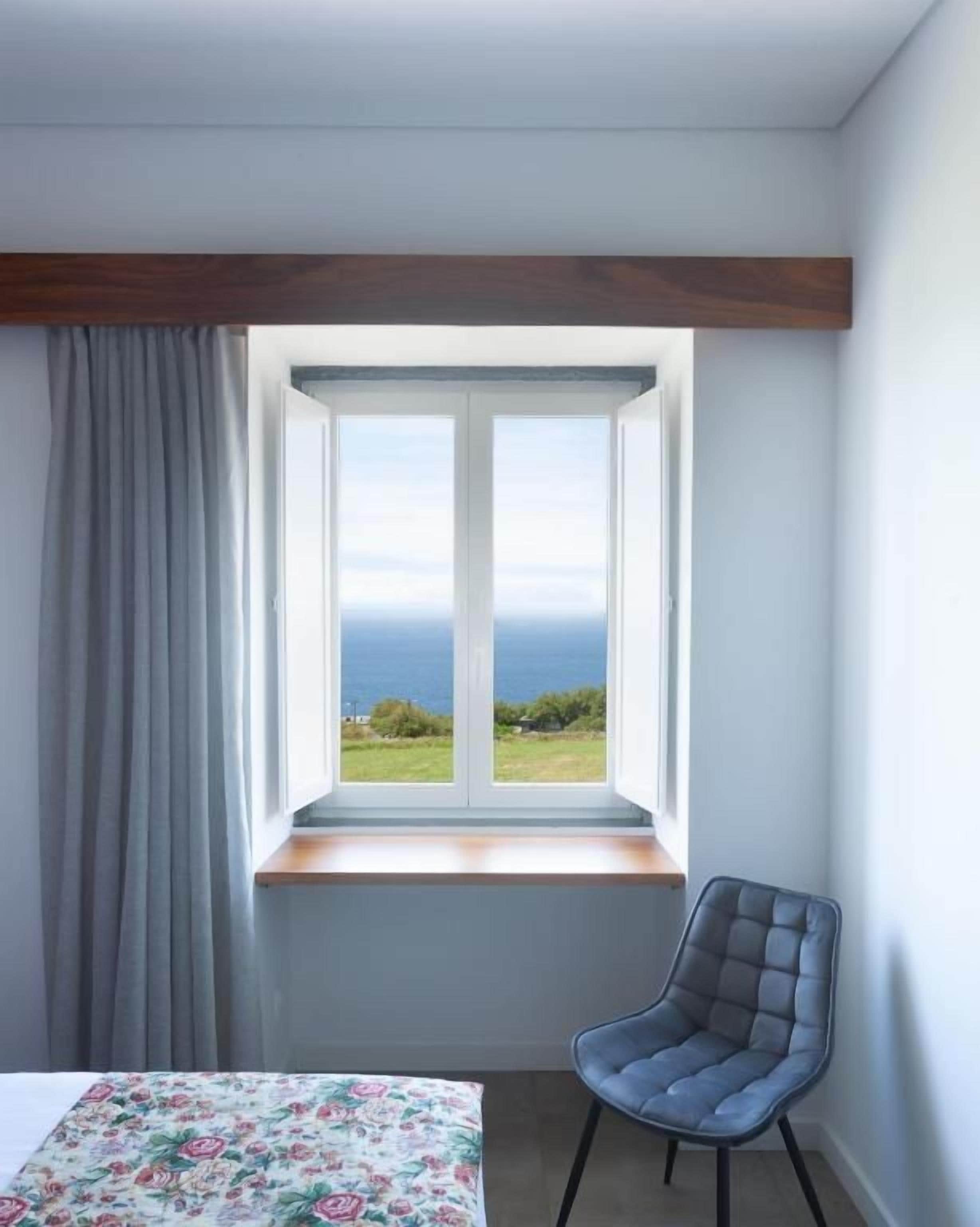 A room with a window, a chair, and a bed with a floral bedspread.