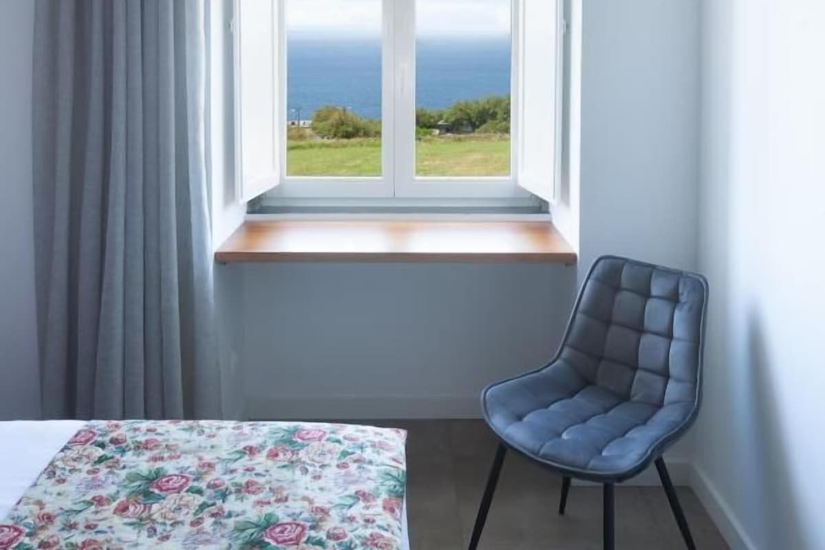 A room with a window, a chair, and a bed with a floral bedspread.