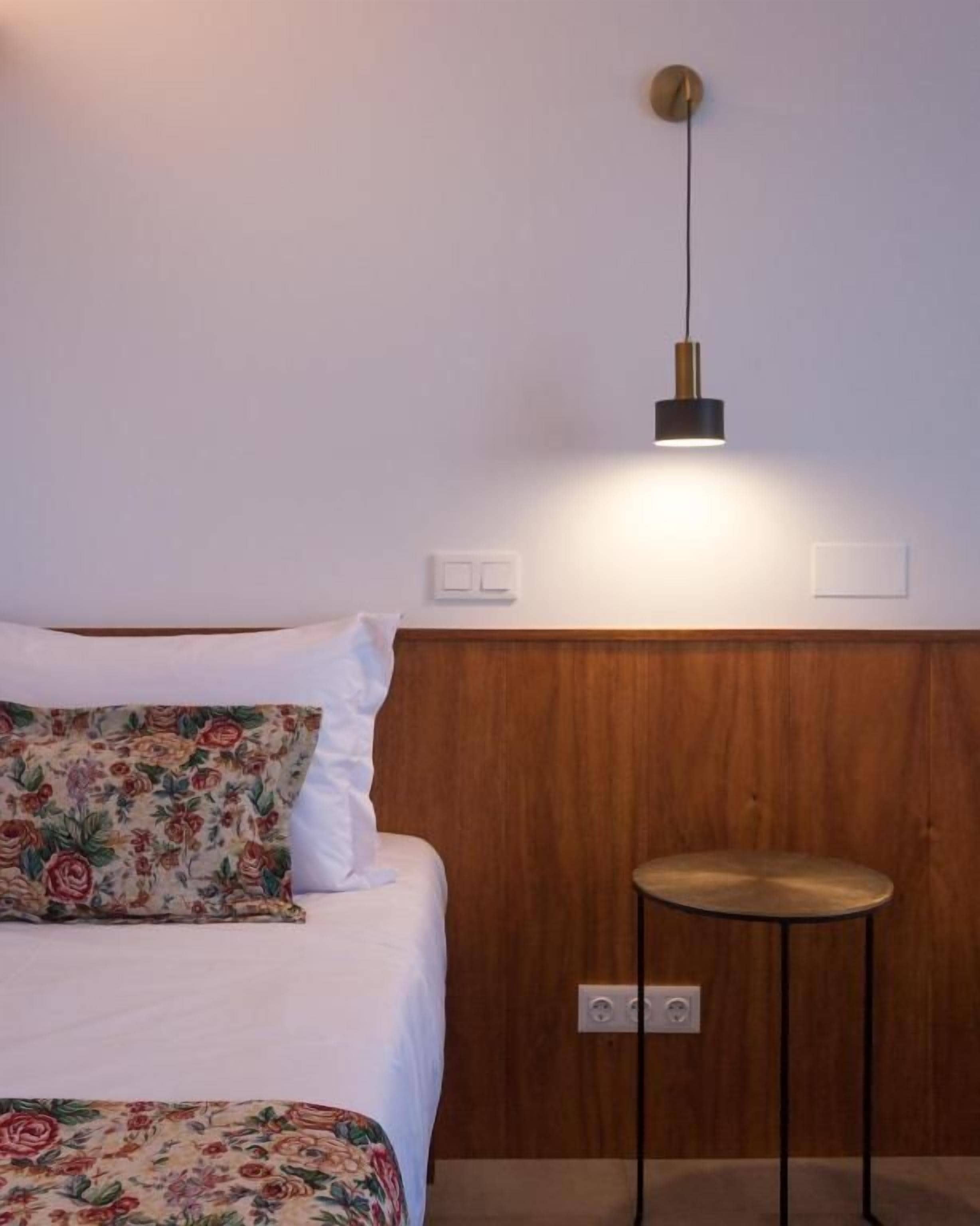 Un dormitorio con cama, mesita de noche, lámpara de pared y toma de corriente.