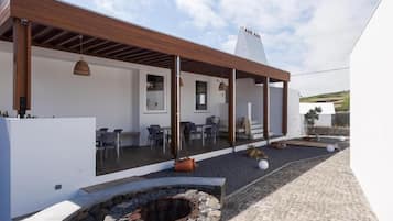 Un patio moderno al aire libre con un pozo de fuego de piedra, una pérgola de madera y una zona de estar.