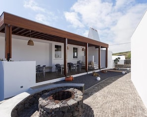 A modern outdoor patio with a stone fire pit, wooden pergola, and seating area. - Casa dos Romeiros (SANTA BARBARA)