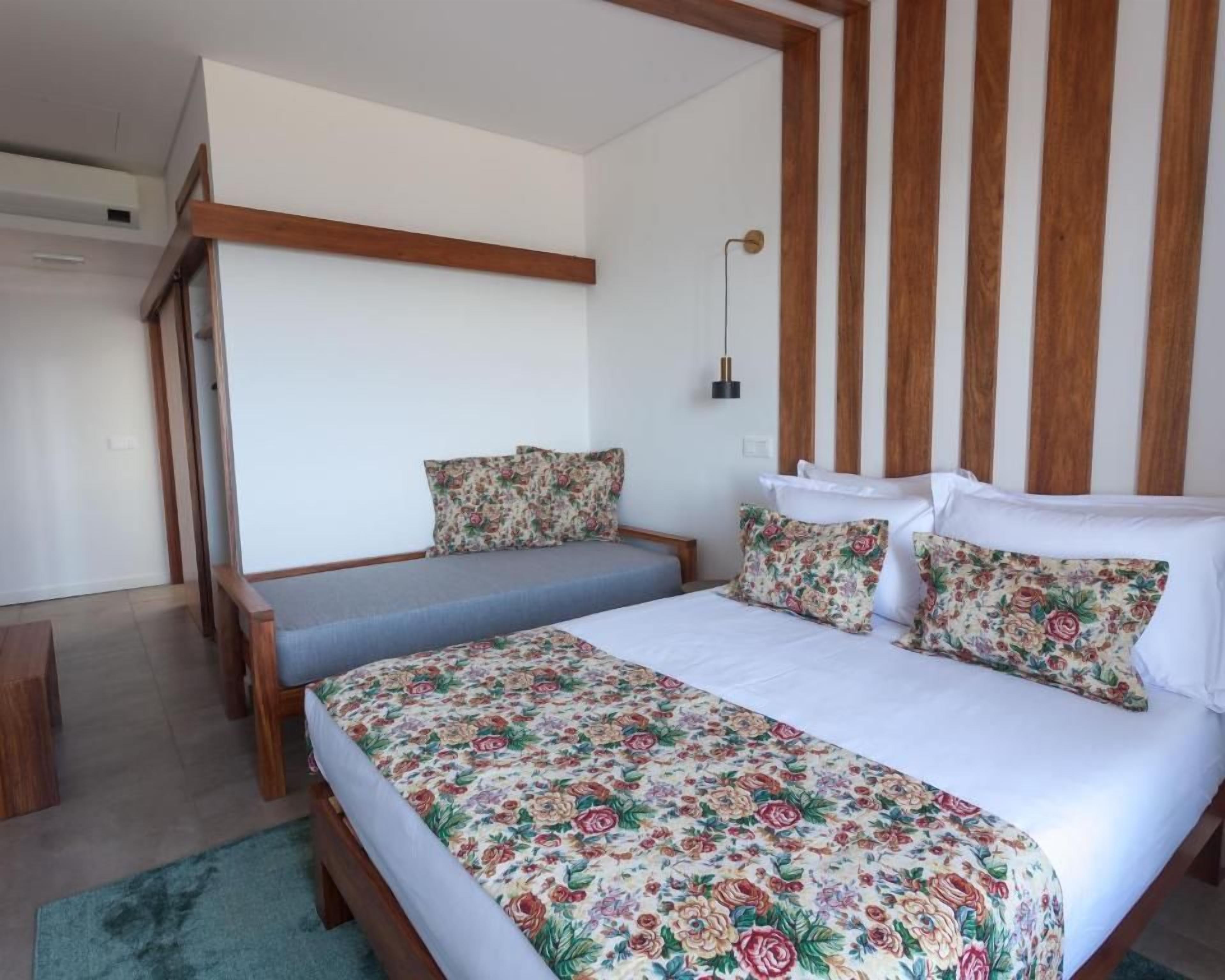 Un dormitorio con cama, un banco y una lámpara fijada a la pared.