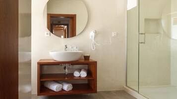 Un baño moderno con un espejo redondo, un tocador de madera, cabina de ducha de vidrio y toallas enrolladas cuidadosamente.