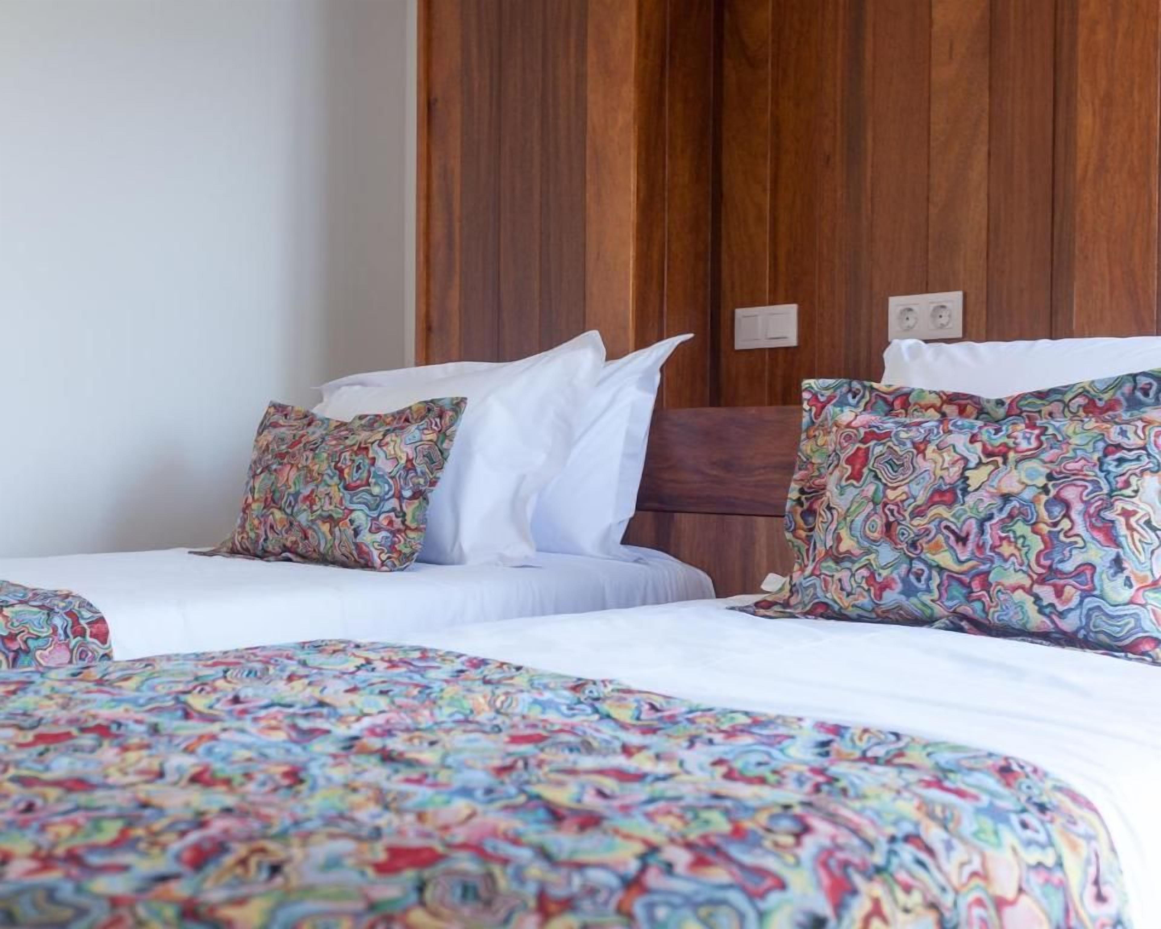 Ein Hotelzimmer mit zwei Betten, jeweils mit gemusterten Bettbezügen und Kissen, und einem Holzschrank im Hintergrund.