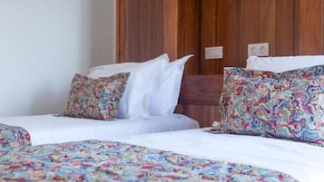 Ein Hotelzimmer mit zwei Betten, jeweils mit gemusterten Bettbezügen und Kissen, und einem Holzschrank im Hintergrund.